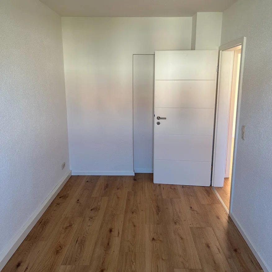 Leerer Raum mit weißen Wänden, Holzboden und einer halb geöffneten weißen Tür.
