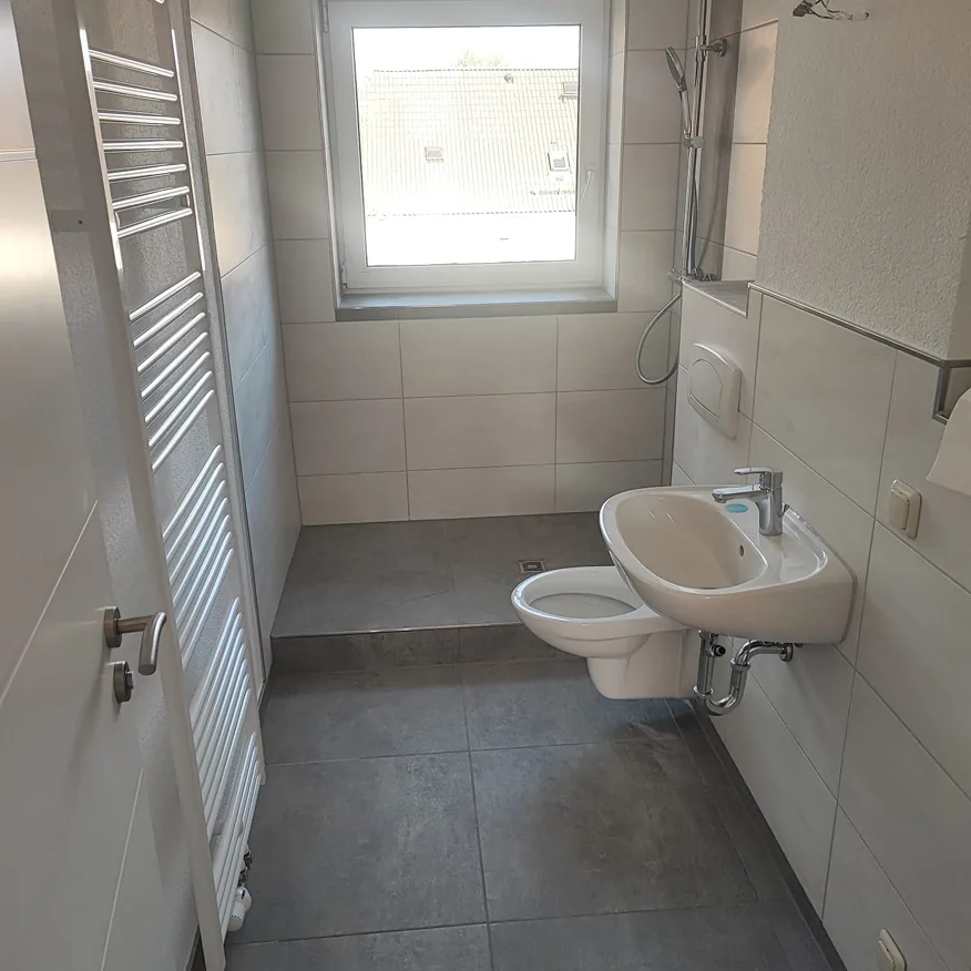 Kleines modernes Badezimmer mit grauen Fliesen, Waschtisch, WC, Dusche und Fenster.